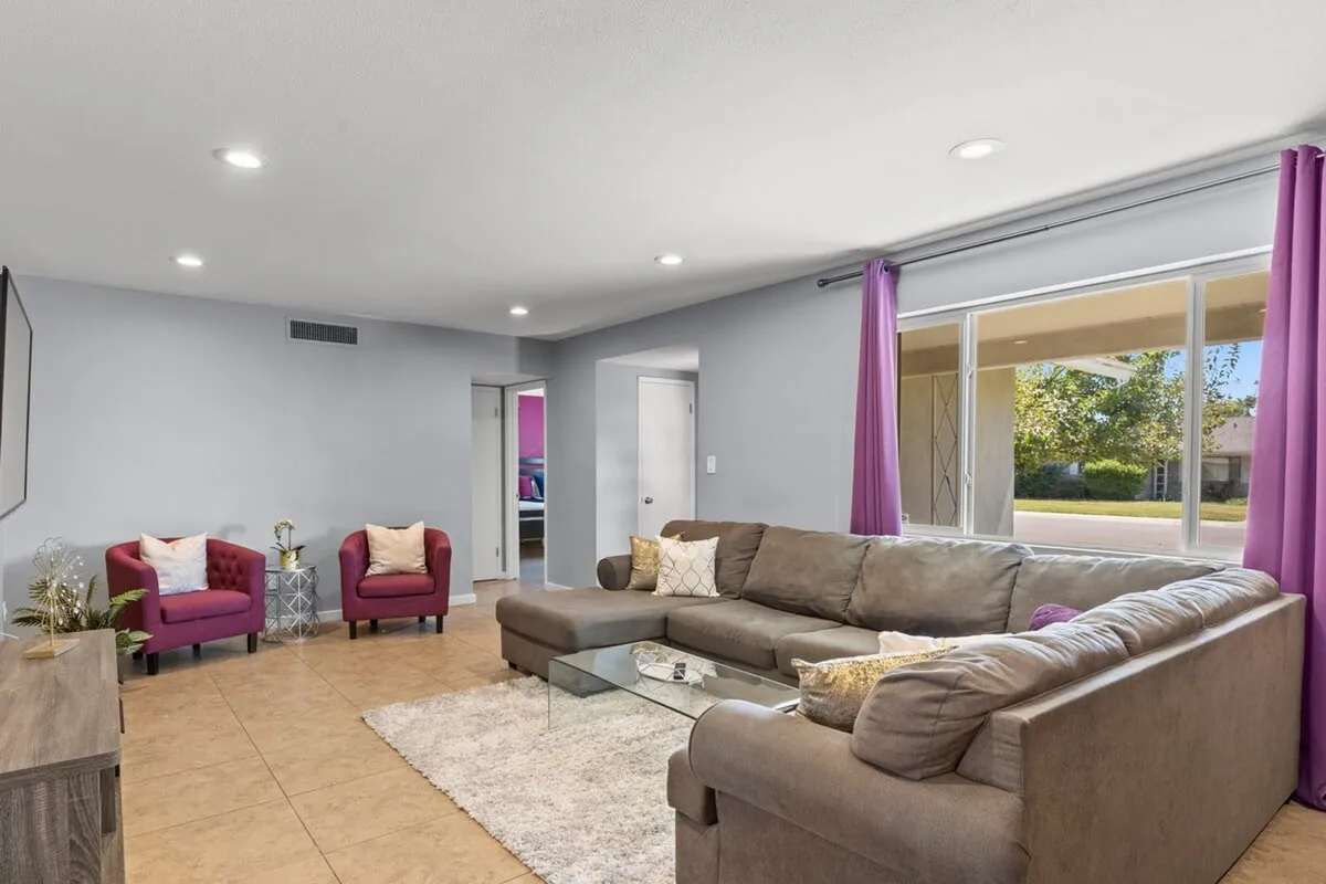 The image showcases a cozy and inviting living area with a plush sofa, vibrant purple curtains, and comfortable armchairs arranged for conversation. The space is well-lit and designed for relaxation or memorable gatherings.