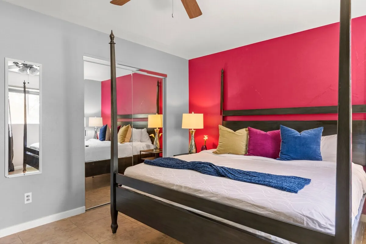 A cozy bedroom featuring a canopy bed with colorful pillows, a mirrored wardrobe, and a nightstand with a lamp. The space exudes comfort and invites relaxation, ideal for restful nights after a busy day.