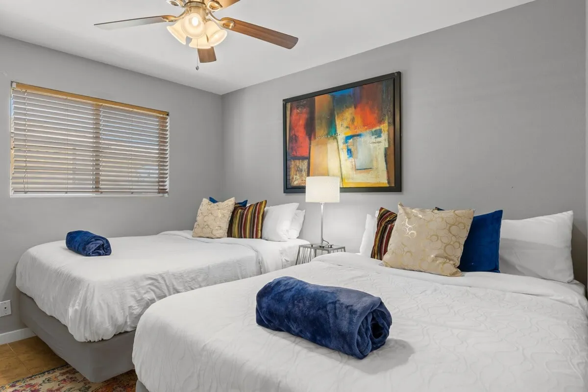 A bedroom with two beds adorned with decorative pillows and a lamp, accompanied by artwork on the wall. The room is bright and welcoming, suitable for friends, teammates, or small family groups.