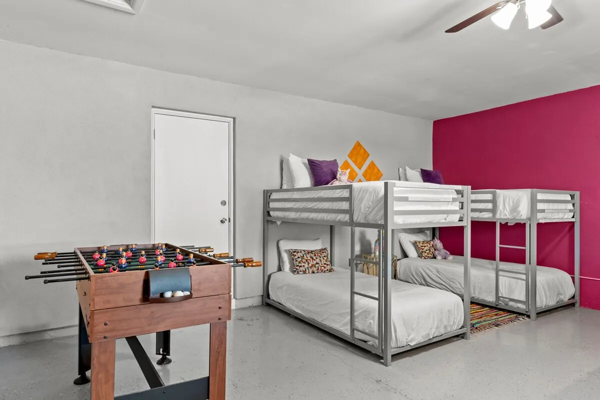 A fun, energetic room with vibrant bunk beds, a foosball table, and a colorful accent wall. The arrangement and playful ambiance suggest a space meant for group fun, friendly games, or cozy sleepovers for kids and adults alike.