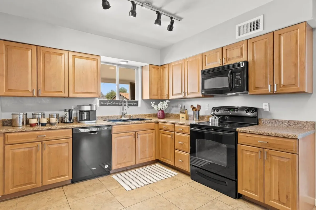 A warm kitchen scene with wooden cabinets, sleek black appliances, a granite countertop, and a kitchen sink, suggesting a fully stocked and functional culinary space ideal for group meals and entertaining.