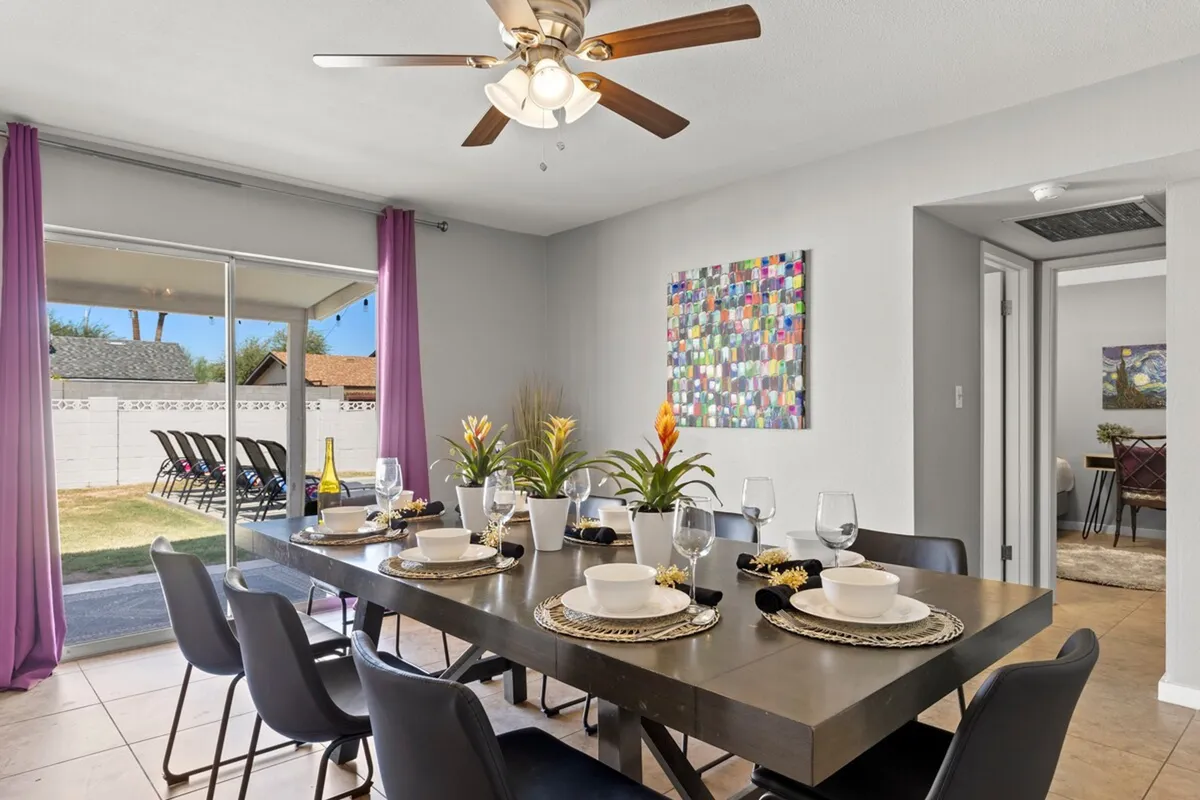 A warm and welcoming dining area featuring a spacious wooden table surrounded by family-sized seating. Colorful artwork adorns the wall, and large windows allow natural light to flood the space, creating an inviting atmosphere for family meals and gatherings.